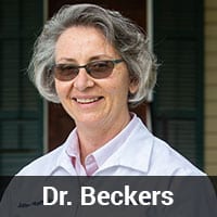 A person with short, gray hair, wearing glasses and a white lab coat, is smiling. There is a dark green shuttered window in the background. The text overlay reads: "Dr. Beckers, Veterinarian.